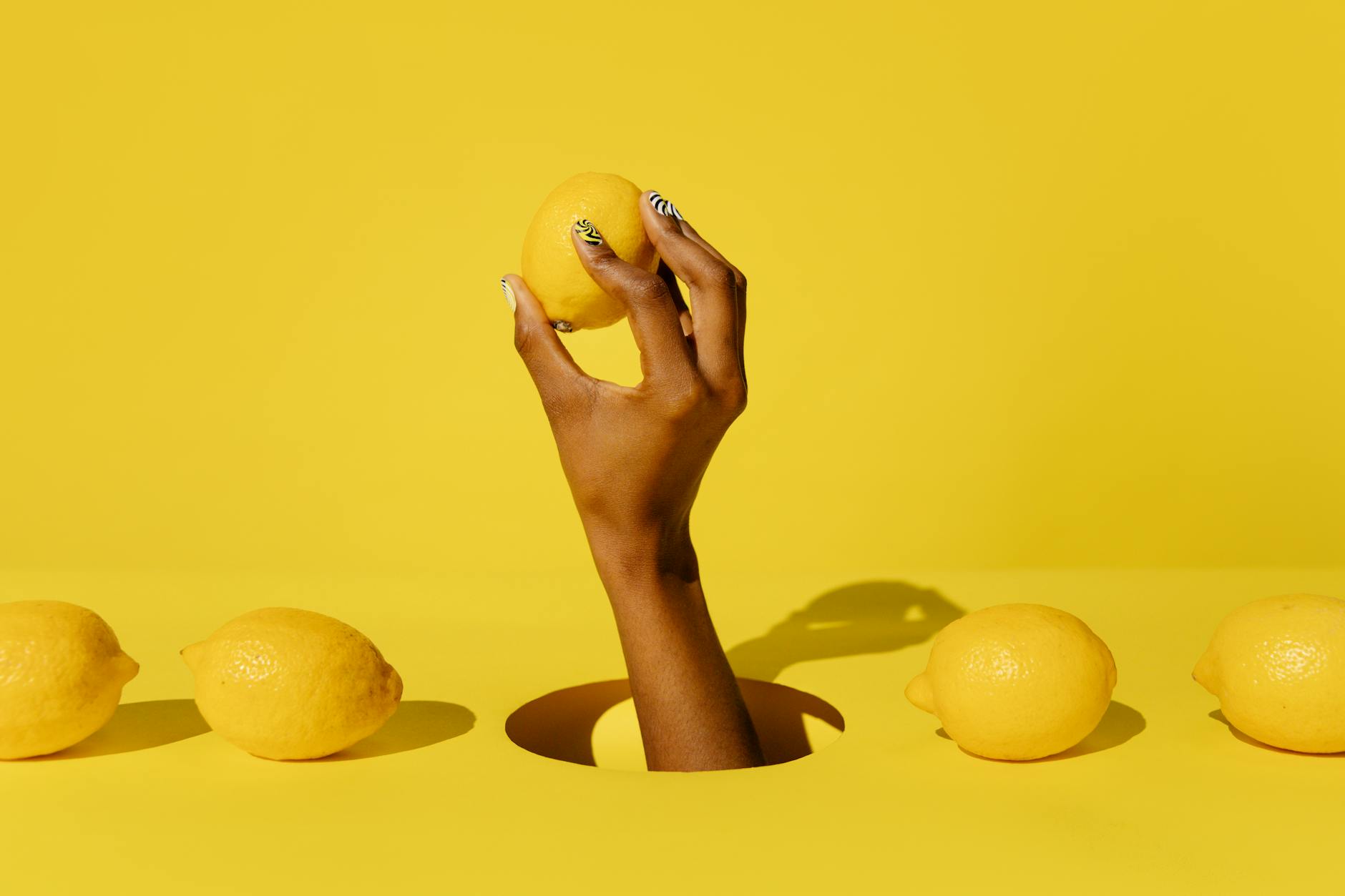 Close-up of a hand holding a lemon vibrator against a minimalistic purple backdrop