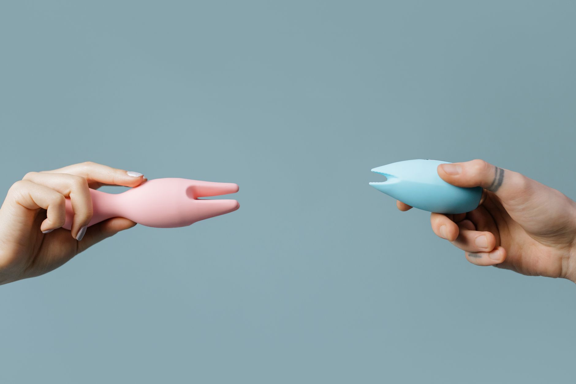 A hand holding a modern orange vibrator against a minimalist purple background