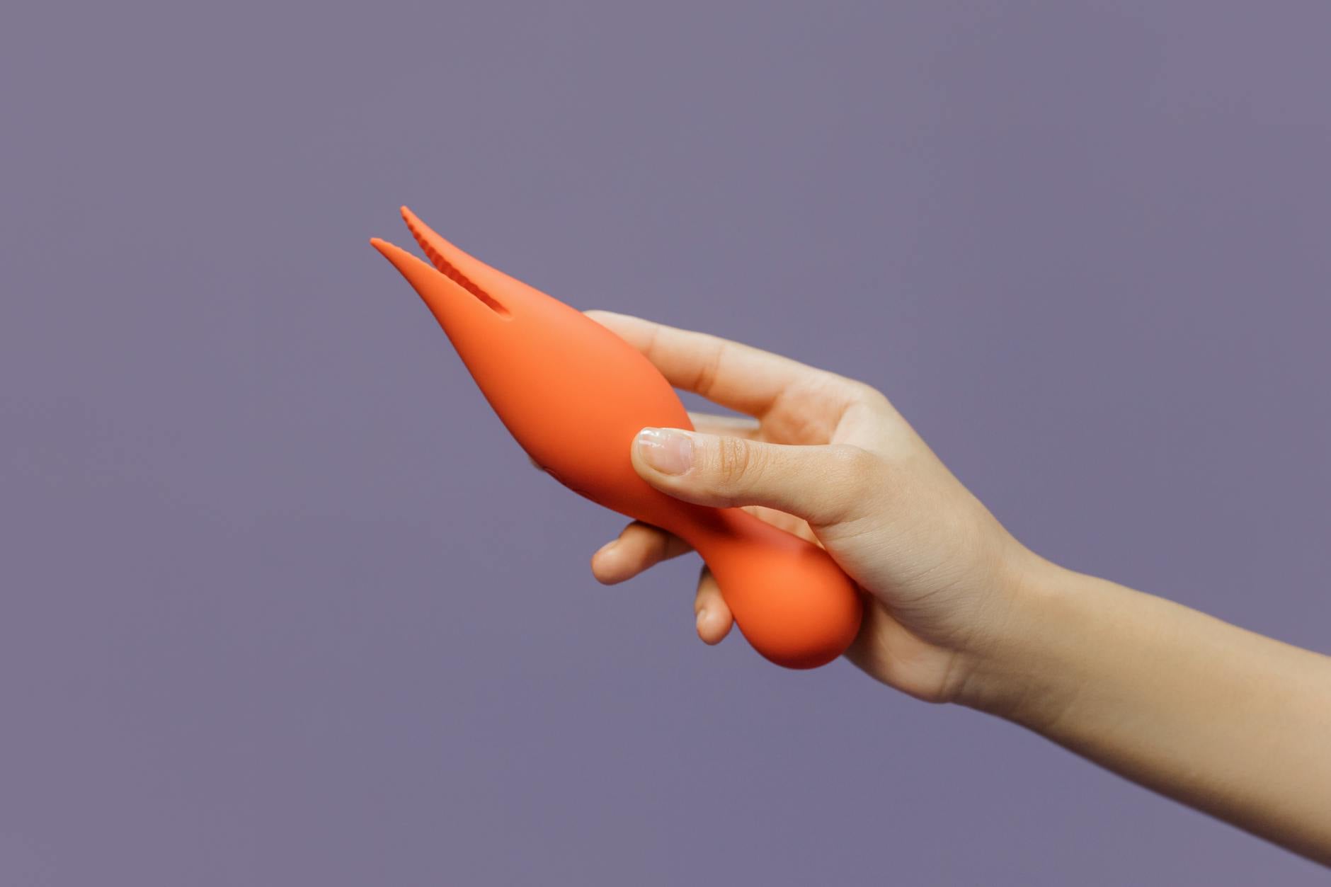 Una mano che tiene un vibratore arancione contro uno sfondo minimalista viola, mostrando la sensualità moderna