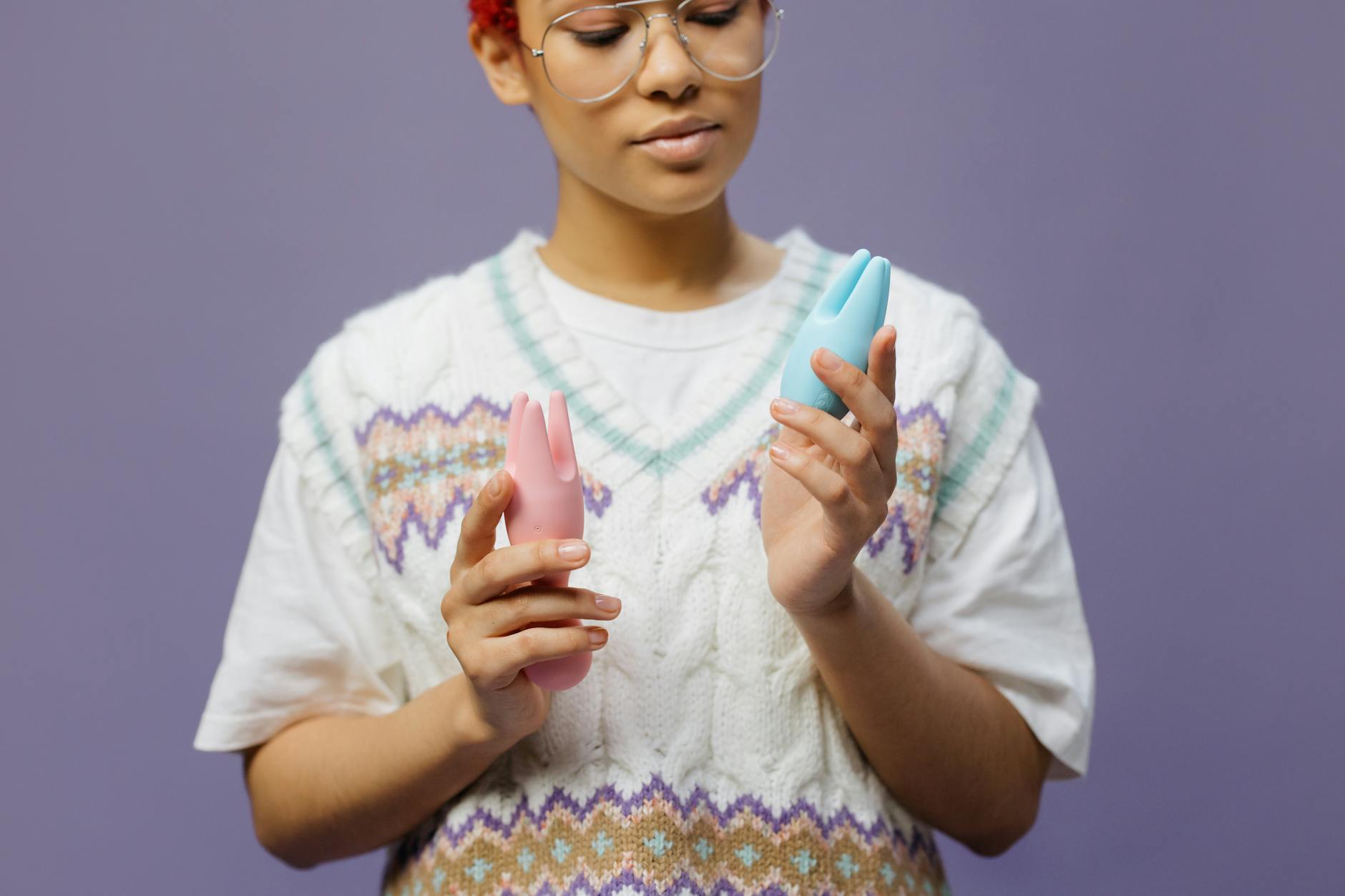 Woman holding pink and blue vibrators thoughtfully during recovery journey
