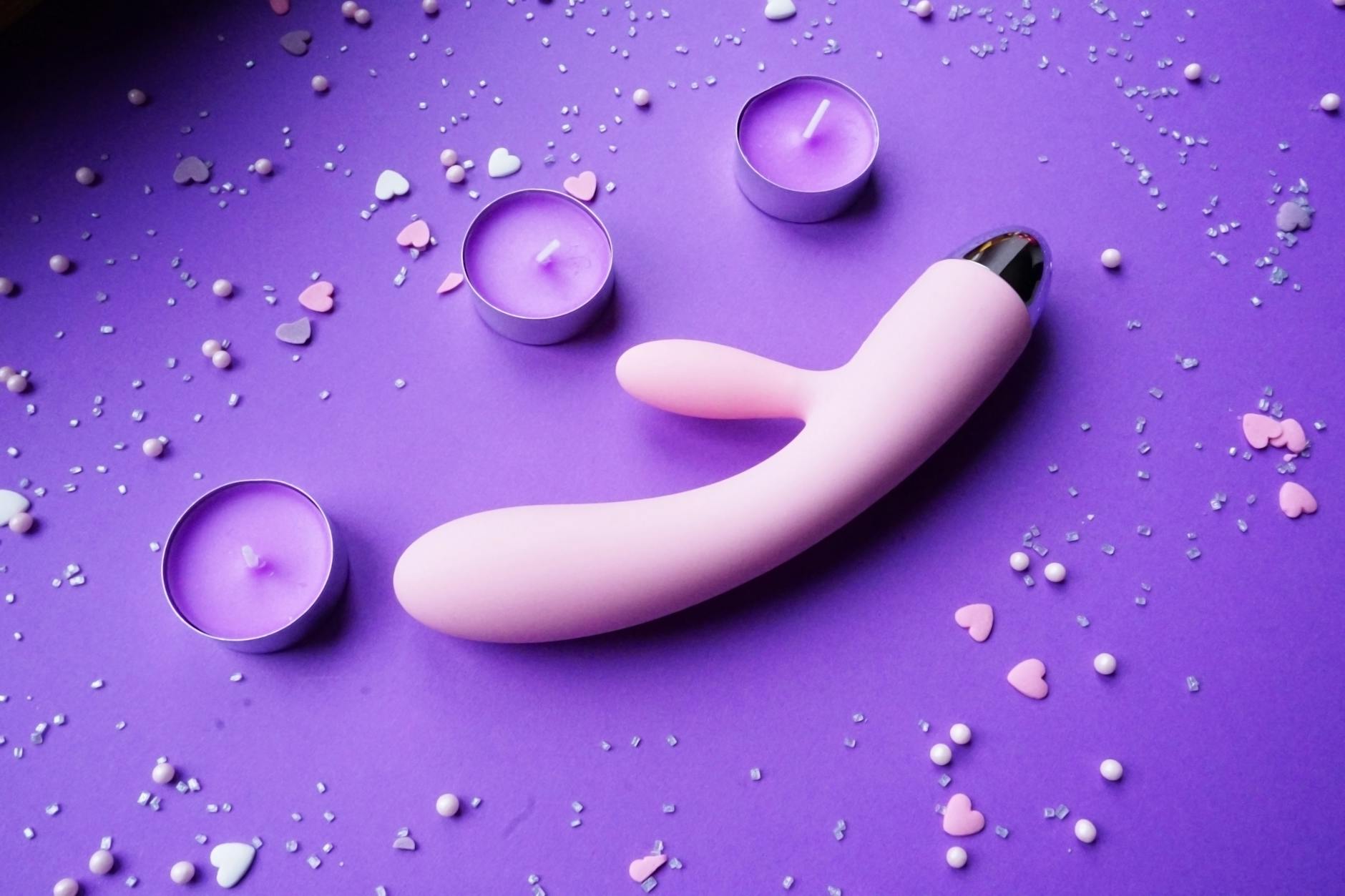 Pink vibrator on purple background with heart confetti and candles for romantic pleasure